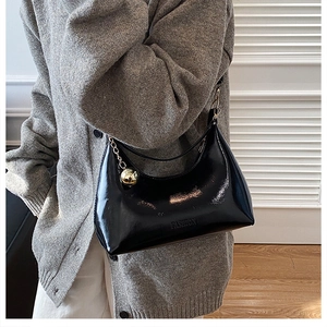 Detailed view of black patent leather crescent hobo bag with gold chain and sphere
