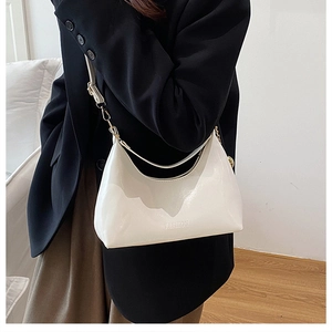 Close-up of white patent leather hobo bag with embossed fashion text and gold buckle detail
