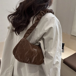 Brown pleated shoulder bag with silver bow detail shown on a model for winter fashion