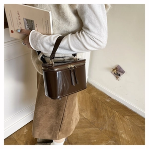 Detail view of the glossy brown patent leather vanity bag with gold-tone dual zippers