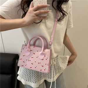Pink cherry print crossbody bag with top handles shown in a mirror selfie lifestyle shot
