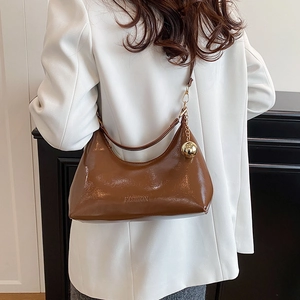 Brown patent leather crescent bag with gold charm worn by model in white suit