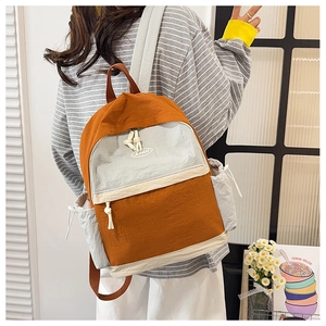 Detail of a color-block backpack in orange and grey with side drawstring pockets