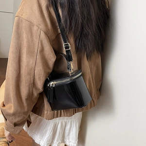 Glossy black patent leather box bag with gold zipper shown on a shoulder-carry model