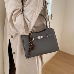 Dark grey litchi grain leather crossbody bag with charms on model wearing beige trench coat