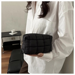 Detail of a black quilted puffer clutch bag featuring square patterns and a gold zipper