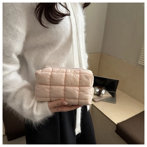 Detail of light pink quilted nylon handbag with top zipper held by a model