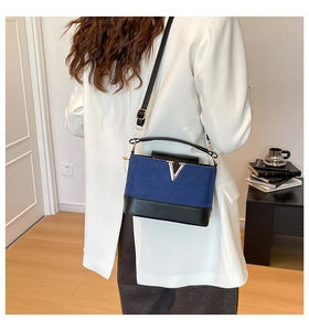 Detail of blue suede bucket bag featuring black leather trim and a golden V-shaped logo