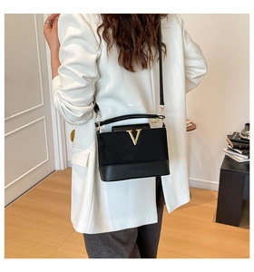 Rear view of a black quilted crossbody bag with gold V buckle on a white blazer