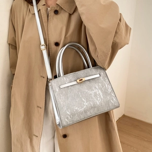 Silver metallic small square handbag with golden twist lock and belt detail on a trench coat
