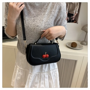 Detail of matte black crossbody bag featuring sweet red cherry charm and adjustable strap