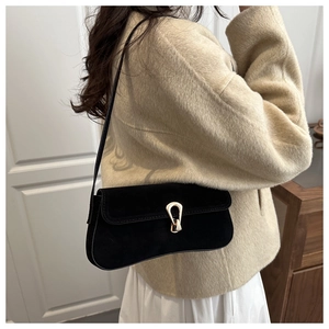 Detail of black suede baguette bag showing the elegant gold clasp and textured finish
