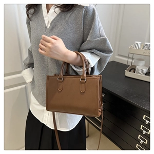 Detail showing the brown textured square handbag with double handles and metal hardware
