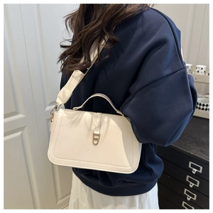 Close-up of cream leather shoulder bag with wide strap and gold buckle detail