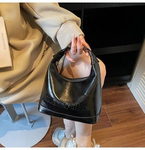 Detail of black glossy handbag with Maison embossing and sleek zipper closure