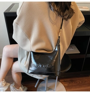 Detail of black glossy leather shoulder bag with maisonhe embossed lettering and strap