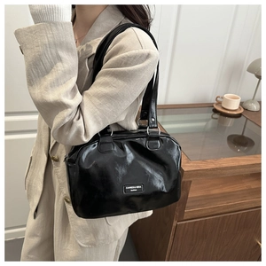 Detail of a black glossy PU leather Boston bag shown on a model in a minimalist setting
