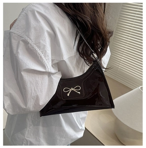 Detail shot of a dark brown patent leather baguette bag with a gold bow buckle on model
