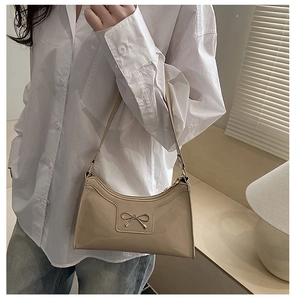 Model wearing a beige glossy patent leather crescent shoulder bag with bow buckle detail
