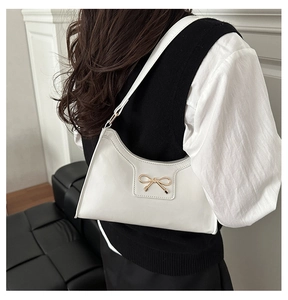 Side view of a white crescent shoulder bag with golden bow clasp worn by a model