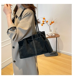 Detail of black suede tote bag with contrast stitching on model with beige coat