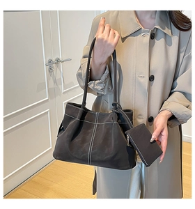 Detail of dark coffee suede shoulder bag with white contrast stitching on beige trench coat