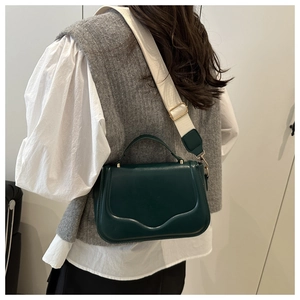 Detail of dark green crossbody bag with cream wide strap worn over a grey vest