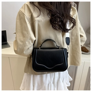 Detail of black crossbody bag featuring round top handle and wide white shoulder strap