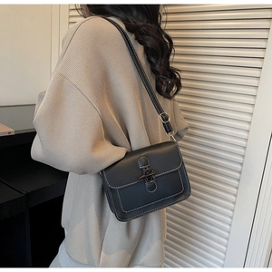Detail of black vintage crossbody bag with white stitching and metal buckle on beige sweater