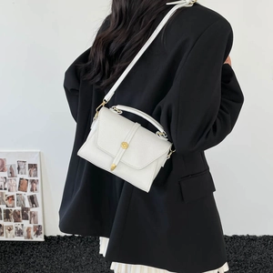 Modella che indossa una borsa in pelle litchi bianca con fibbia dorata su blazer nero