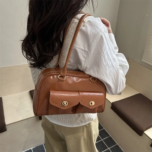 Sac à bandoulière marron brillant avec deux poches avant et boucles dorées sur modèle