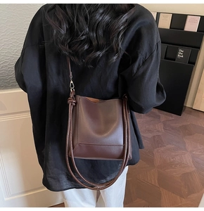 Detail of dark brown leather bucket bag with knot decor on a model in a minimalist room