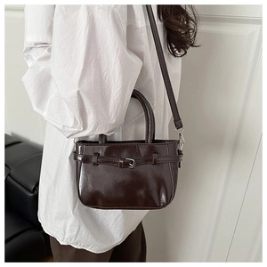 Detail of dark brown glossy leather handbag with belt buckle and metallic hardware