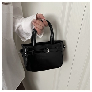 Detail of a mini black patent leather handbag with silver buckle and glossy finish