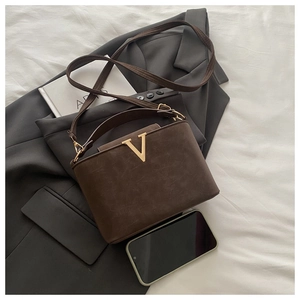Detailed close-up of brown matte leather shoulder bag with a gold metal V-logo on a blazer