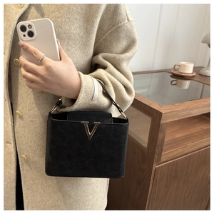 Close-up of black leather handbag with a golden V-shaped metal hardware and top handle
