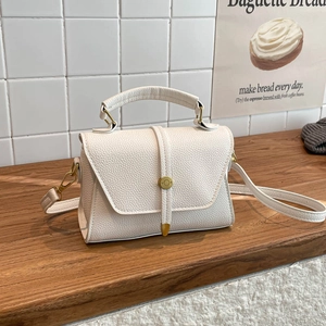 Elegant white litchi pattern leather handbag with metal round buckle on wooden table