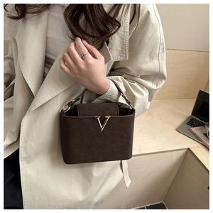 Detail of dark brown leather handbag with gold V-shaped clasp held by model in trench coat