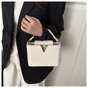 Close-up of white bucket bag with gold V-shaped hardware worn with a black blazer