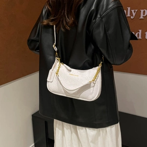 Sac hobo blanc avec texture autruche et chaîne dorée porté par un mannequin en noir