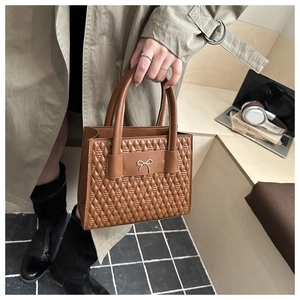 Close-up of brown quilted faux leather handbag with golden bow detail and top handles