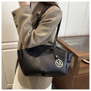 Detail of black leather tote bag featuring a round gold metal M-letter charm tag