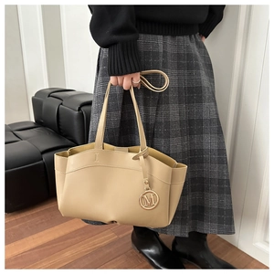 Detail of a beige leather tote bag with a golden M letter pendant in a lifestyle setting