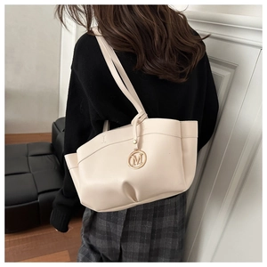Detail of cream tote bag with gold M-letter charm and elegant side pleat design