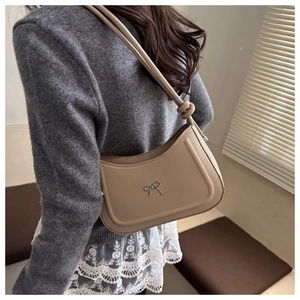 Detail shot of apricot underarm bag featuring a metallic silver bow on smooth faux leather