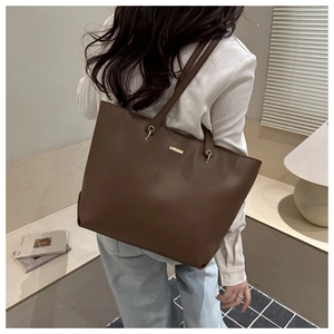 Detail of minimalist dark brown matte leather tote bag with thin straps and gold metal plaque
