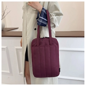 Close-up of a burgundy quilted tote bag with padded geometric lines and zipper closure