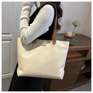 Detailed side view of large cream tote bag with brown leather strap and metal logo