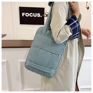 Detail of light blue quilted nylon tote bag worn by model in minimalist indoor setting