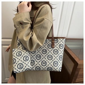Detailed view of monogram print tote and matching pouch set worn with a trench coat